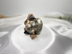 Treasured Energies large polished Ocean Jasper crystal heart held by a small platypus figurine on white satin fabric.