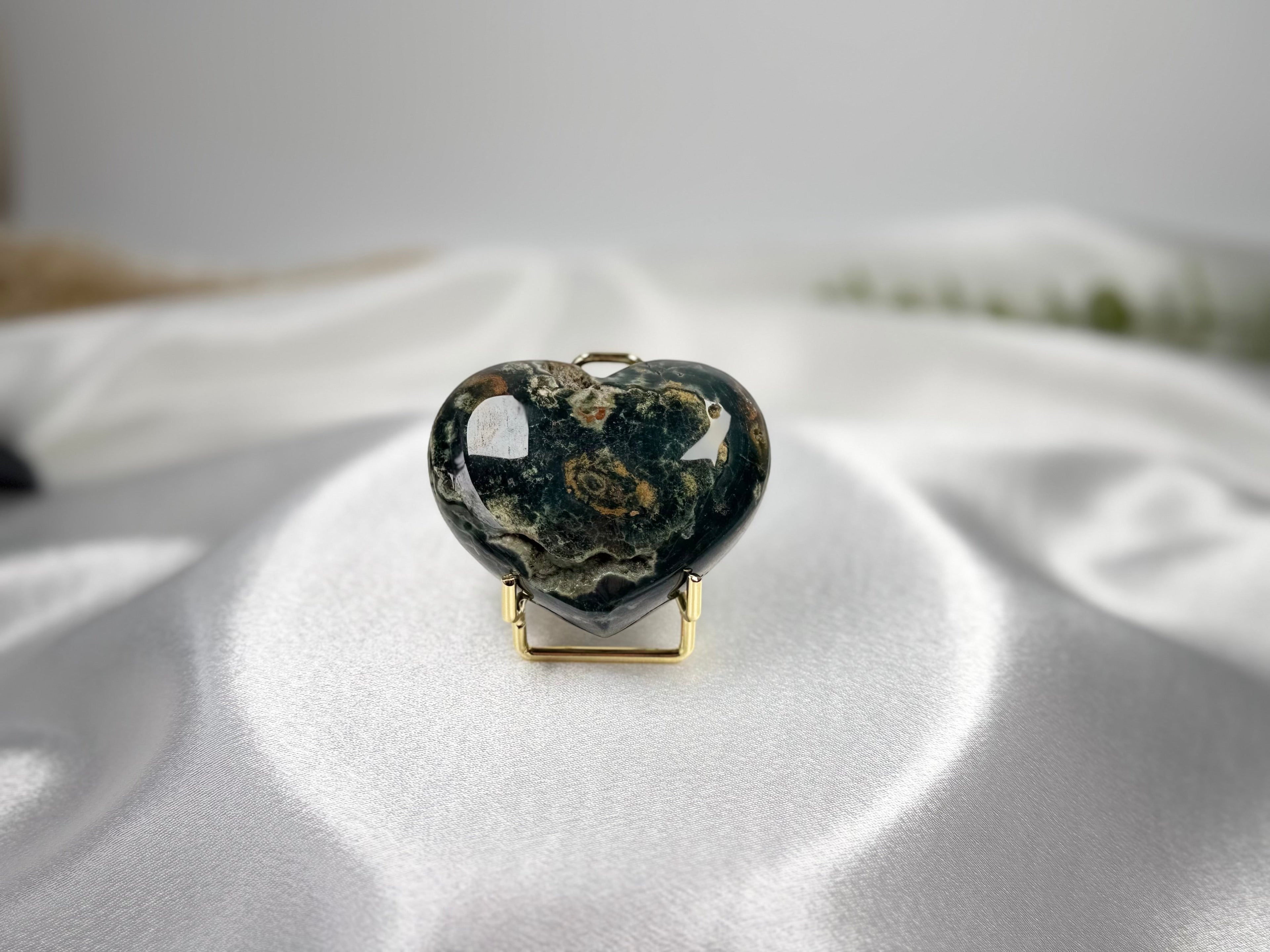 Treasured Energies large heart-shaped Ocean Jasper crystal with dark green and earthy patterns on a white silk cloth.
