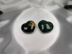 Two Treasured Energies polished Ocean Jasper heart crystals with dark green and gold patterns on white satin fabric.