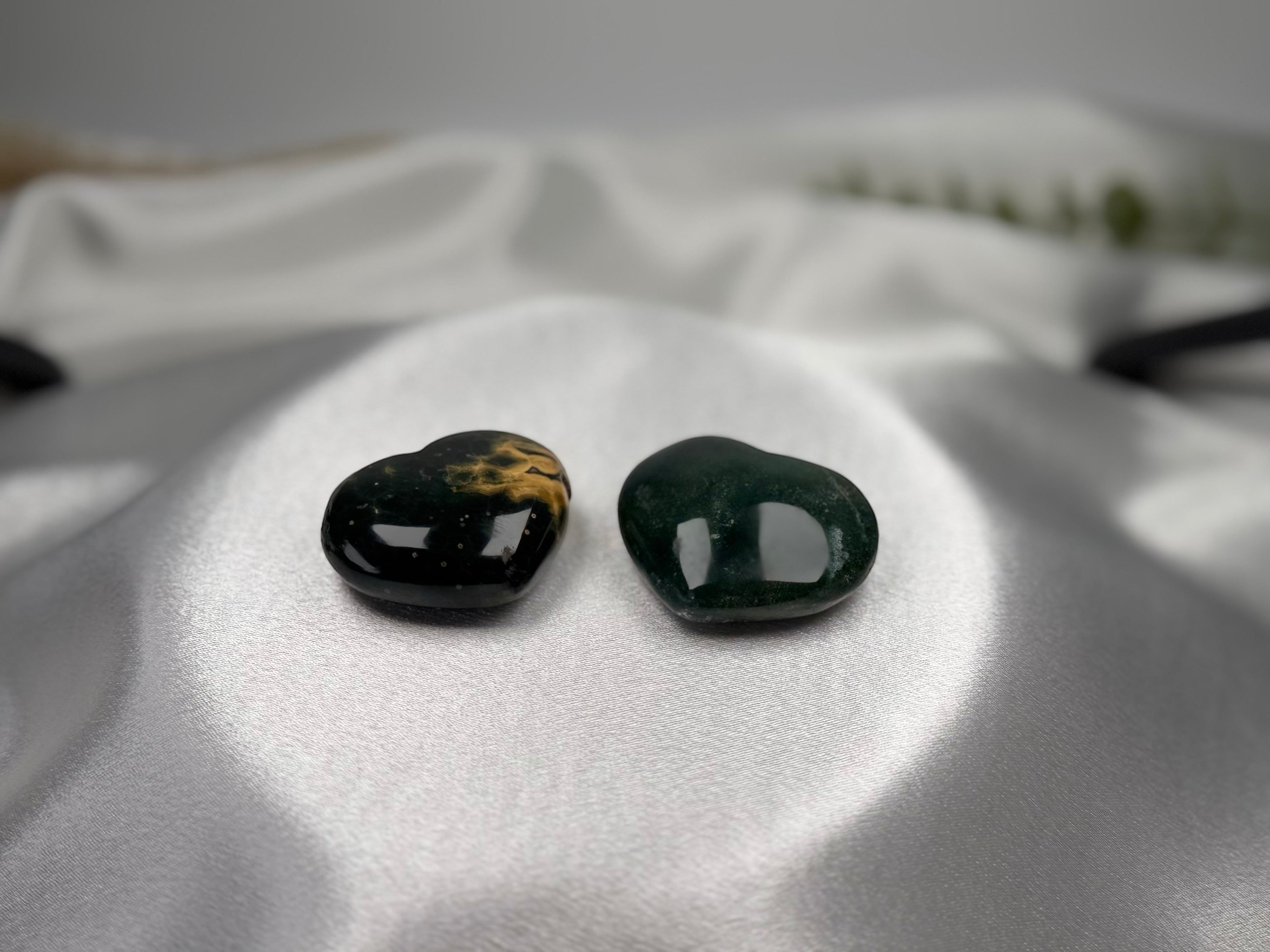 Two Treasured Energies small heart-shaped Ocean Jasper crystals with dark green and gold patterns on white silk.