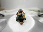 Treasured Energies small heart-shaped Ocean Jasper crystal held by a cute platypus figurine on a white fabric surface.