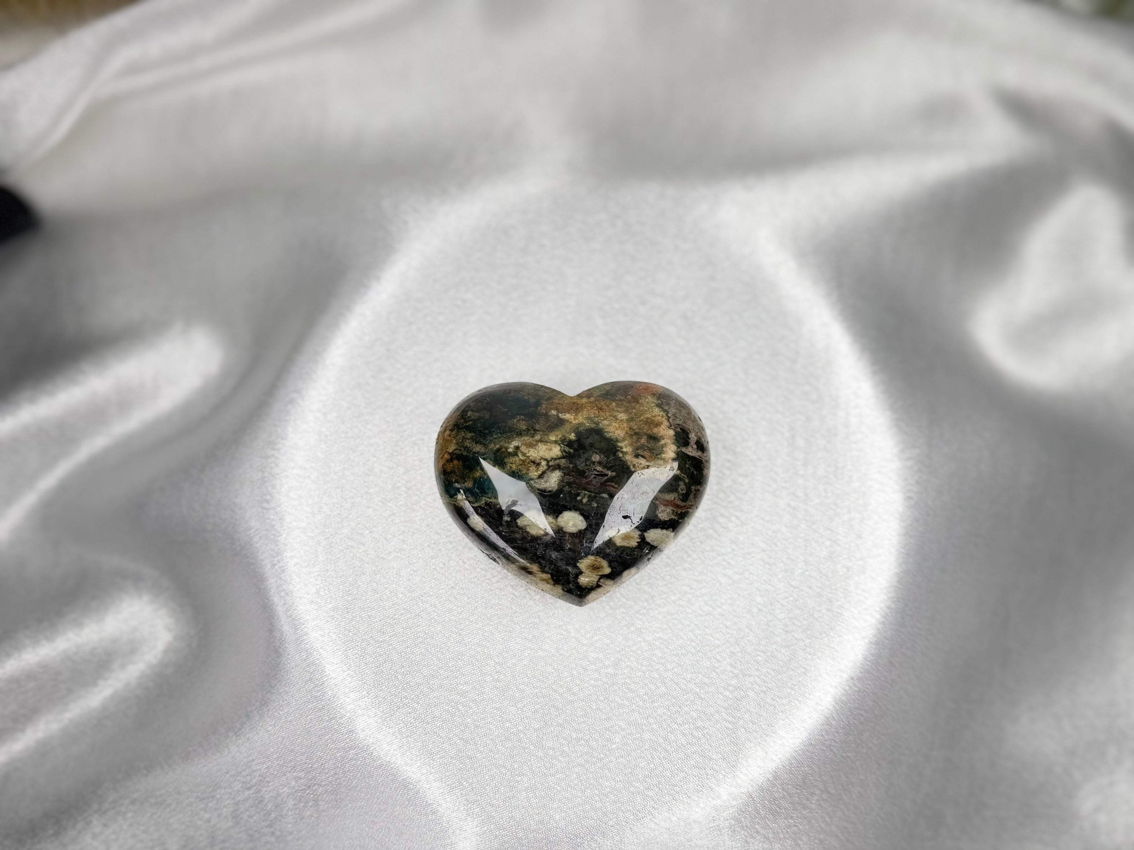 Treasured Energies large polished Ocean Jasper crystal heart with dark green and brown patterns on white satin fabric.