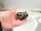 Treasured Energies large polished Ocean Jasper crystal heart held in a hand, showing dark green and tan patterns.