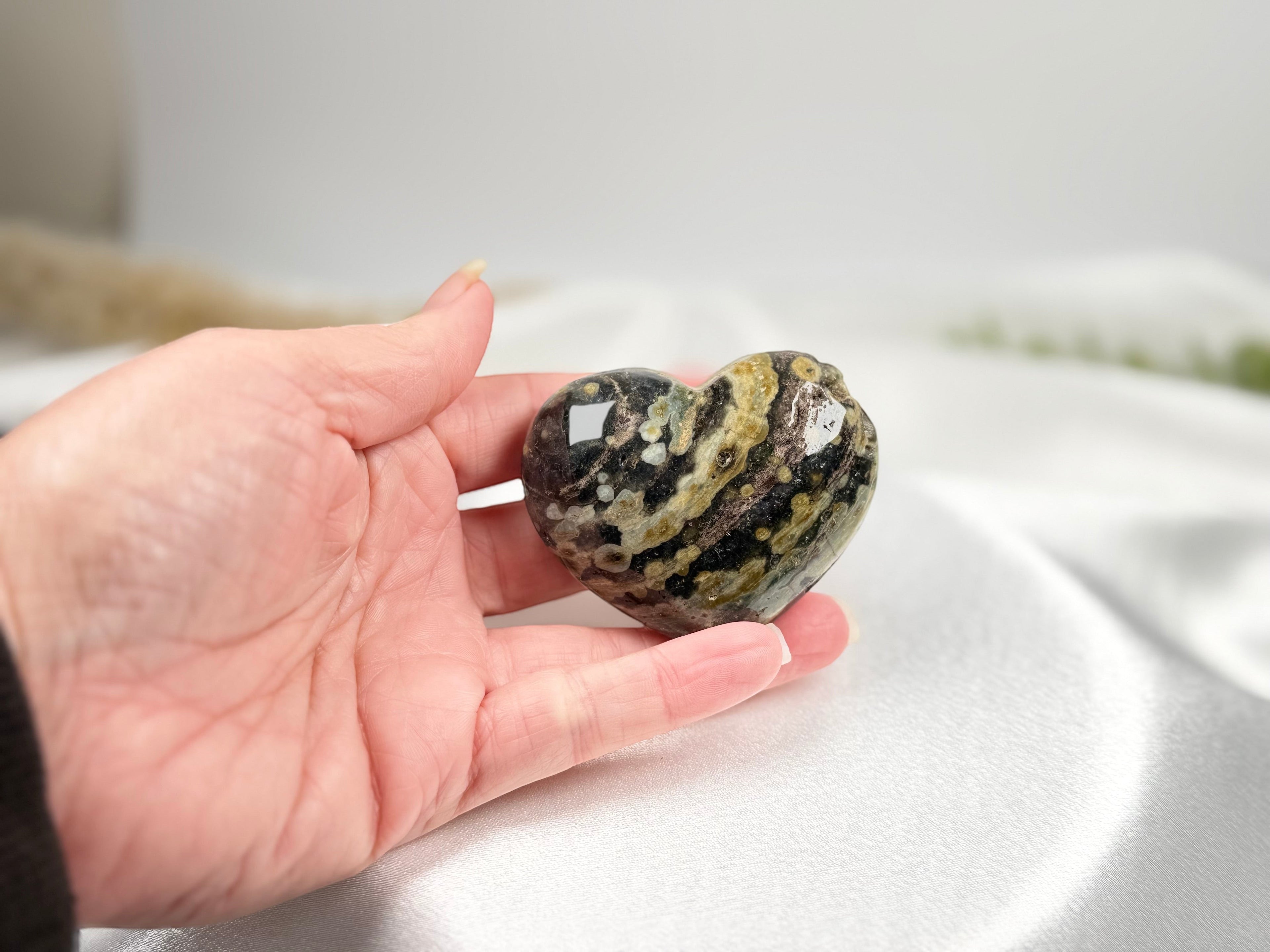 Treasured Energies large polished Ocean Jasper crystal heart held in a hand, showing dark green and tan patterns.