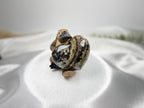 Treasured Energies large polished Ocean Jasper crystal heart held by a small platypus figurine on white satin fabric.