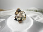 Treasured Energies large polished Ocean Jasper crystal heart held by a small platypus figurine on white satin fabric.