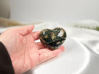 Treasured Energies large polished Ocean Jasper crystal heart held in a hand against a soft white fabric background.