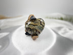 Treasured Energies large polished Ocean Jasper crystal heart held by a small platypus figurine on white satin fabric.
