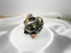 Treasured Energies large polished Ocean Jasper crystal heart held by a small platypus figurine on white satin fabric.