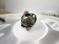 Treasured Energies large polished Ocean Jasper crystal heart held by a small platypus figurine on white satin fabric.