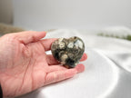 Treasured Energies large polished Ocean Jasper crystal heart held in a palm, showing green and grey orb patterns.