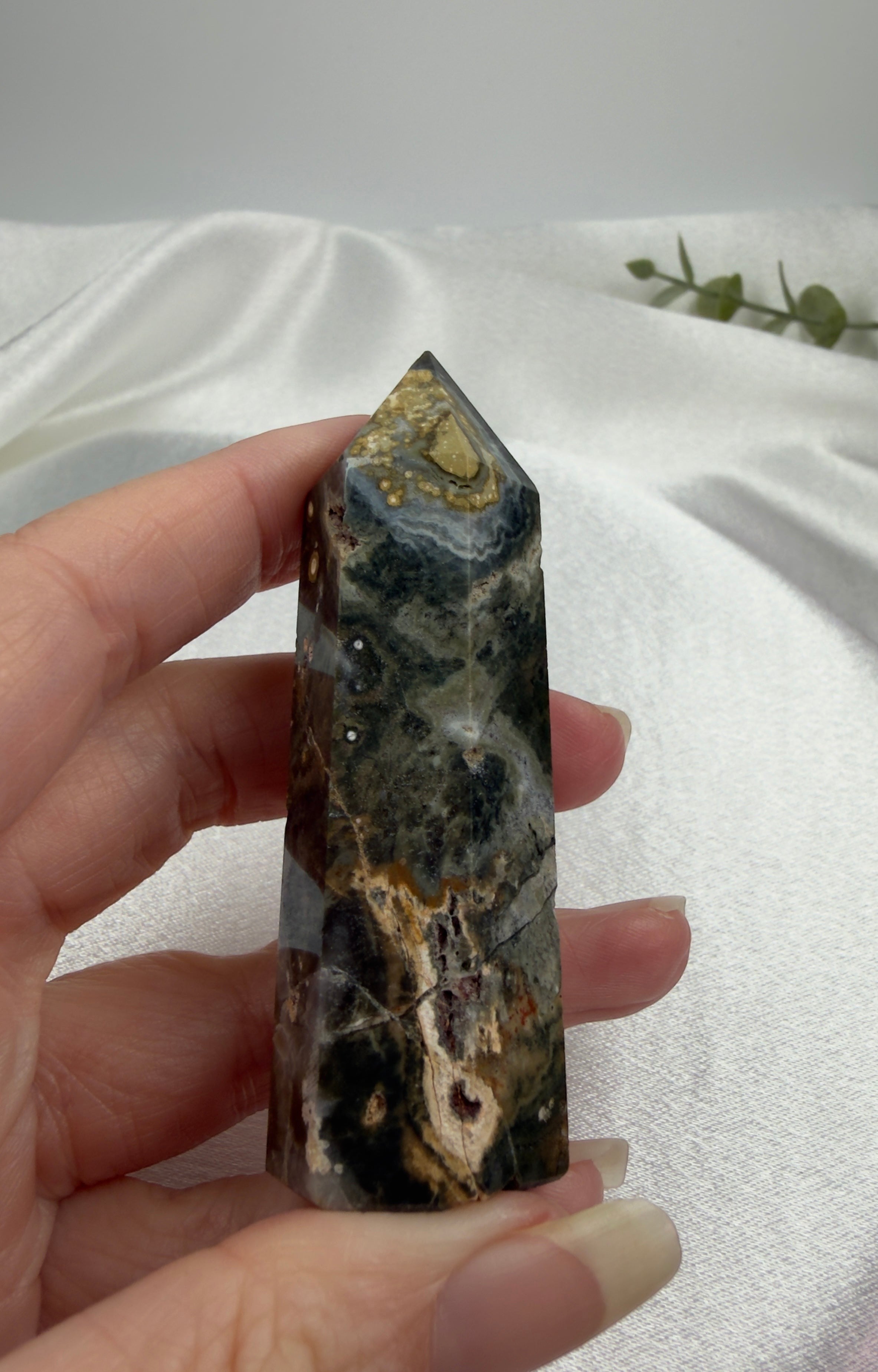 Treasured Energies Ocean Jasper crystal tower with dark green, brown, and cream orbicular patterns held in a hand.