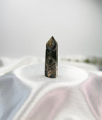 Treasured Energies Ocean Jasper crystal tower with dark green and grey patterns on a white satin fabric background.