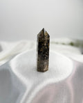 Treasured Energies dark brown Ocean Jasper crystal tower with circular orb patterns on a white satin background.