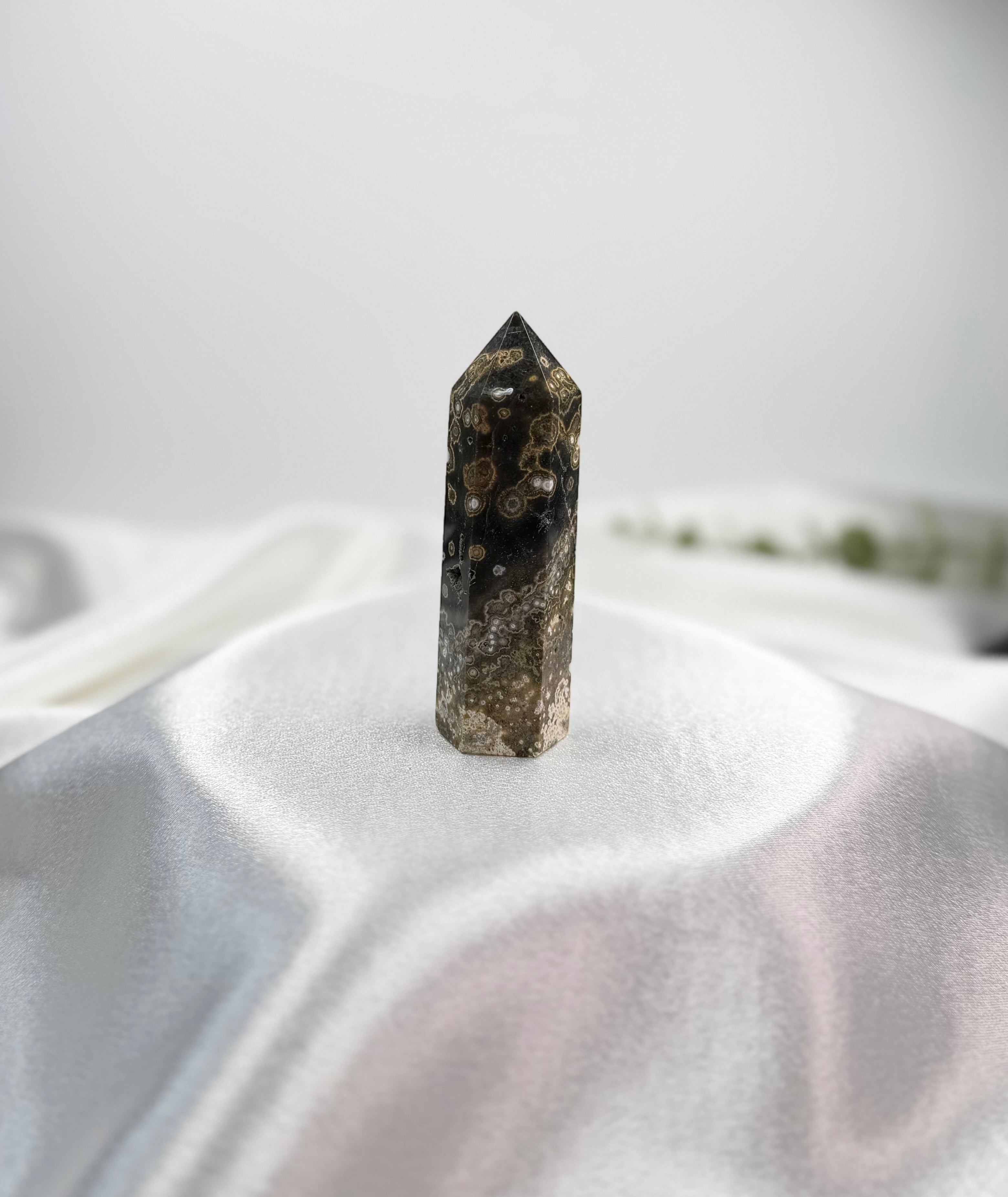 Treasured Energies Ocean Jasper crystal tower with dark brown and cream orbicular patterns on a white silk fabric.
