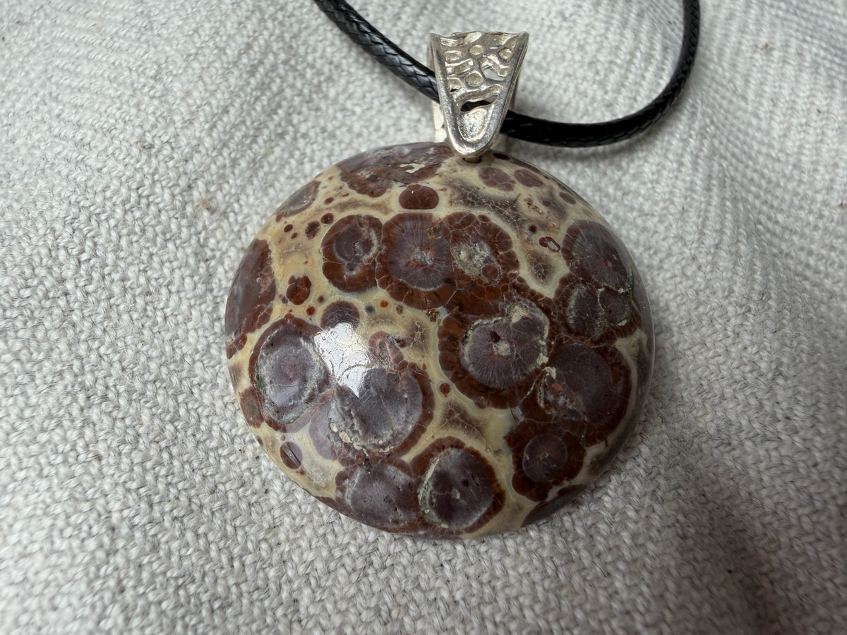 Treasured Energies polished orbicular poppy jasper pendant with brown and tan circular patterns on a black cord necklace.