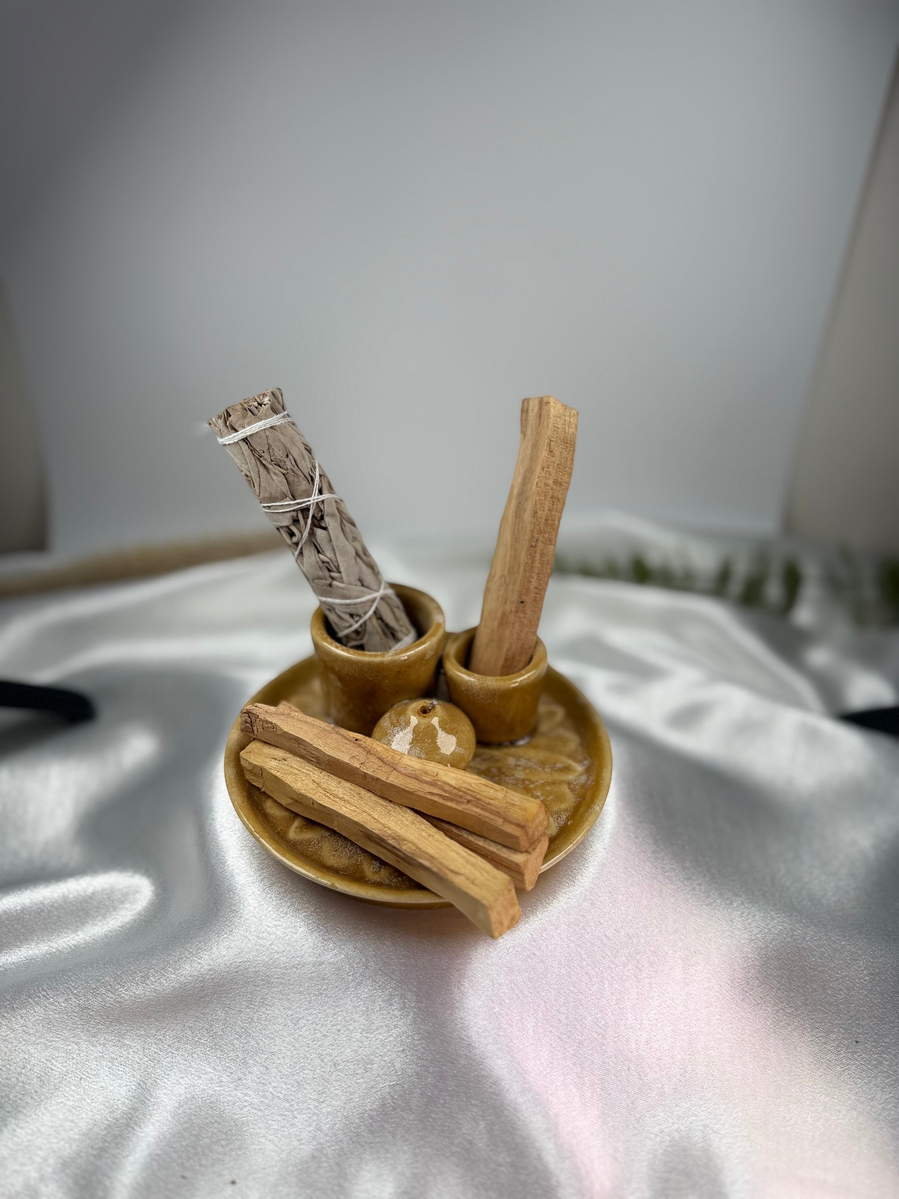 Treasured Energies palo santo sticks and white sage bundle in a small brown ceramic holder on white satin fabric