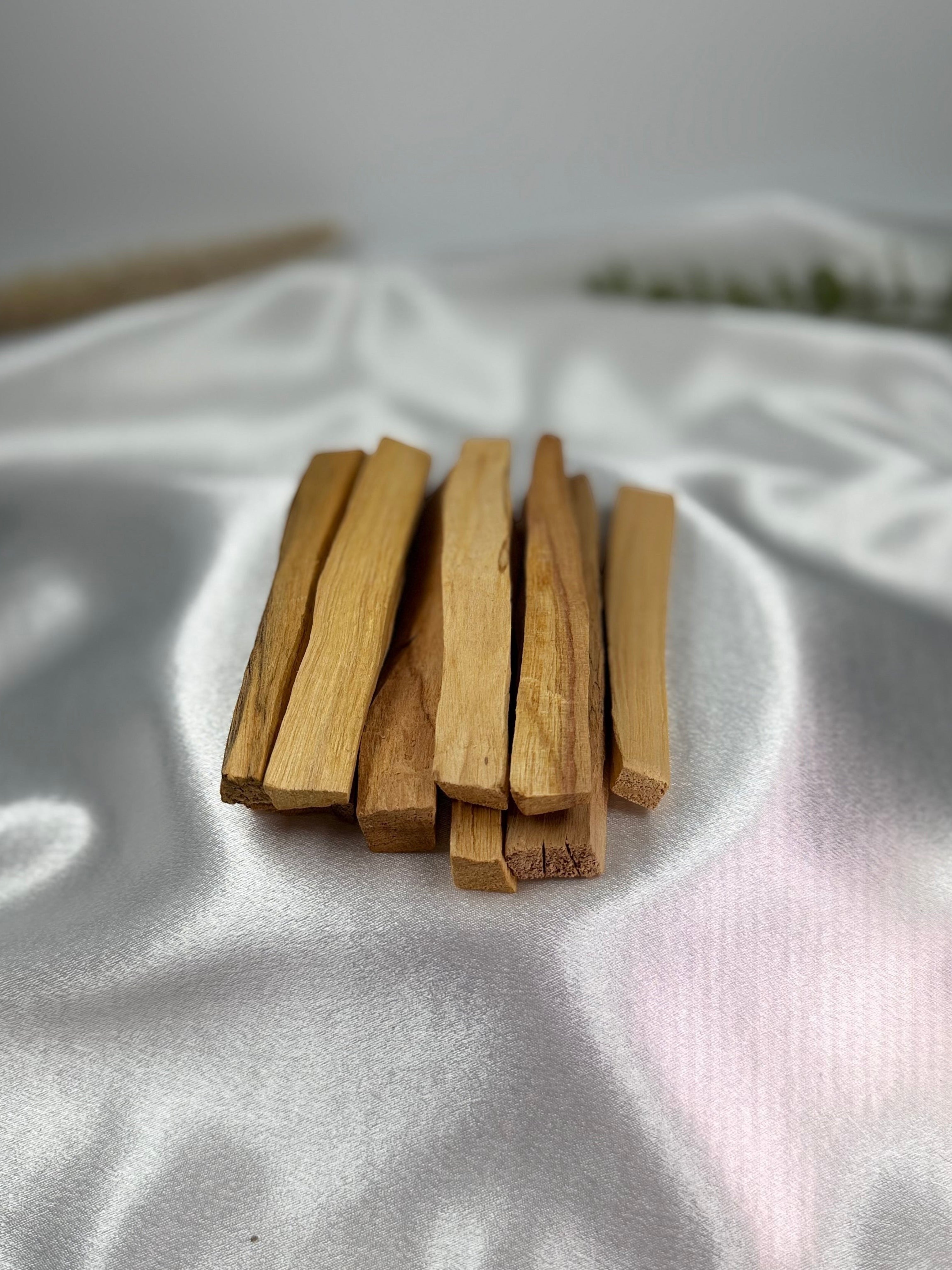 Treasured Energies palo santo sticks arranged on a smooth white satin fabric background