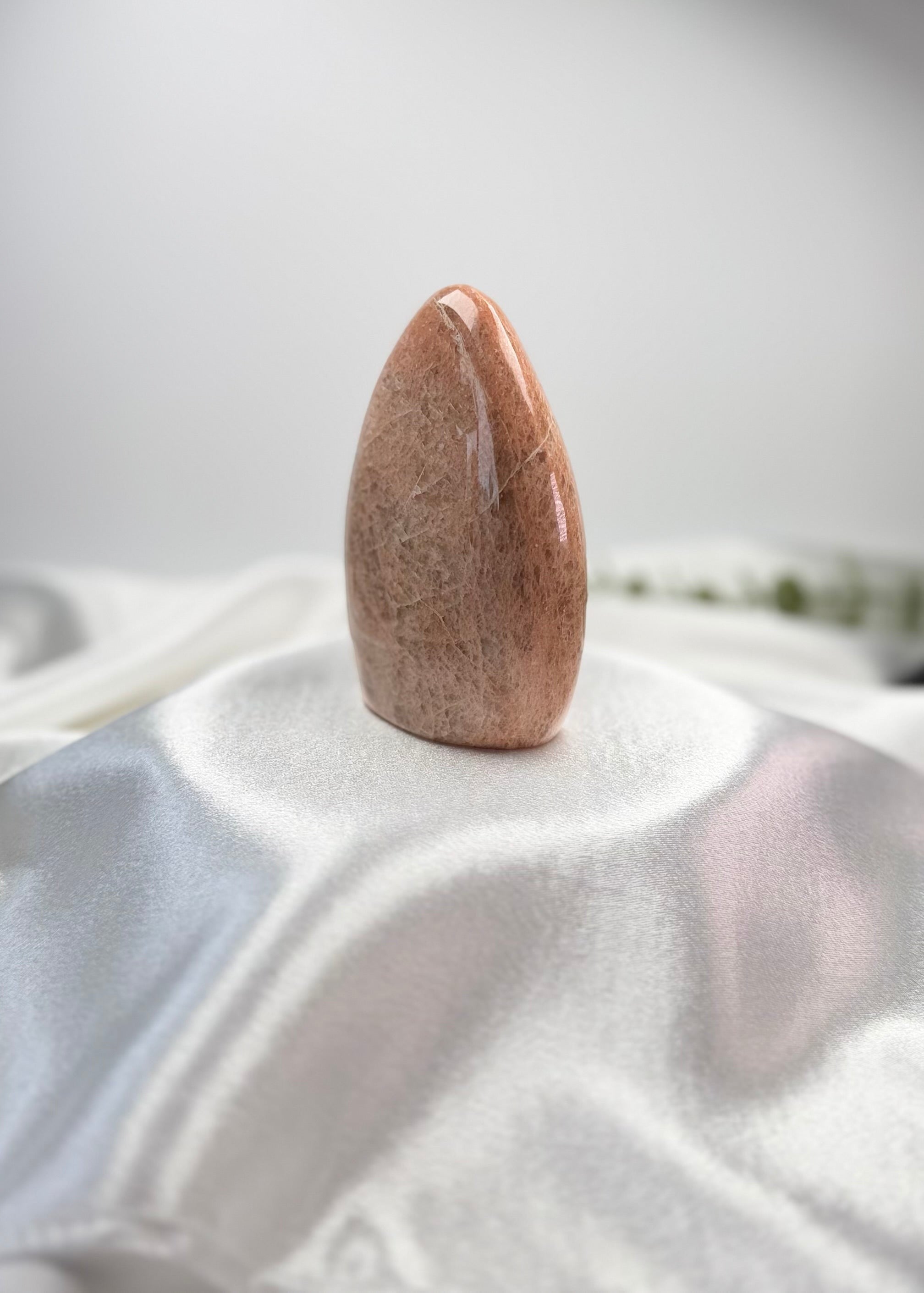 Treasured Energies polished peach moonstone crystal freeform with a smooth, organic shape on a white satin cloth.