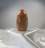 Treasured Energies polished peach moonstone crystal freeform with smooth, organic surface on a white satin fabric.
