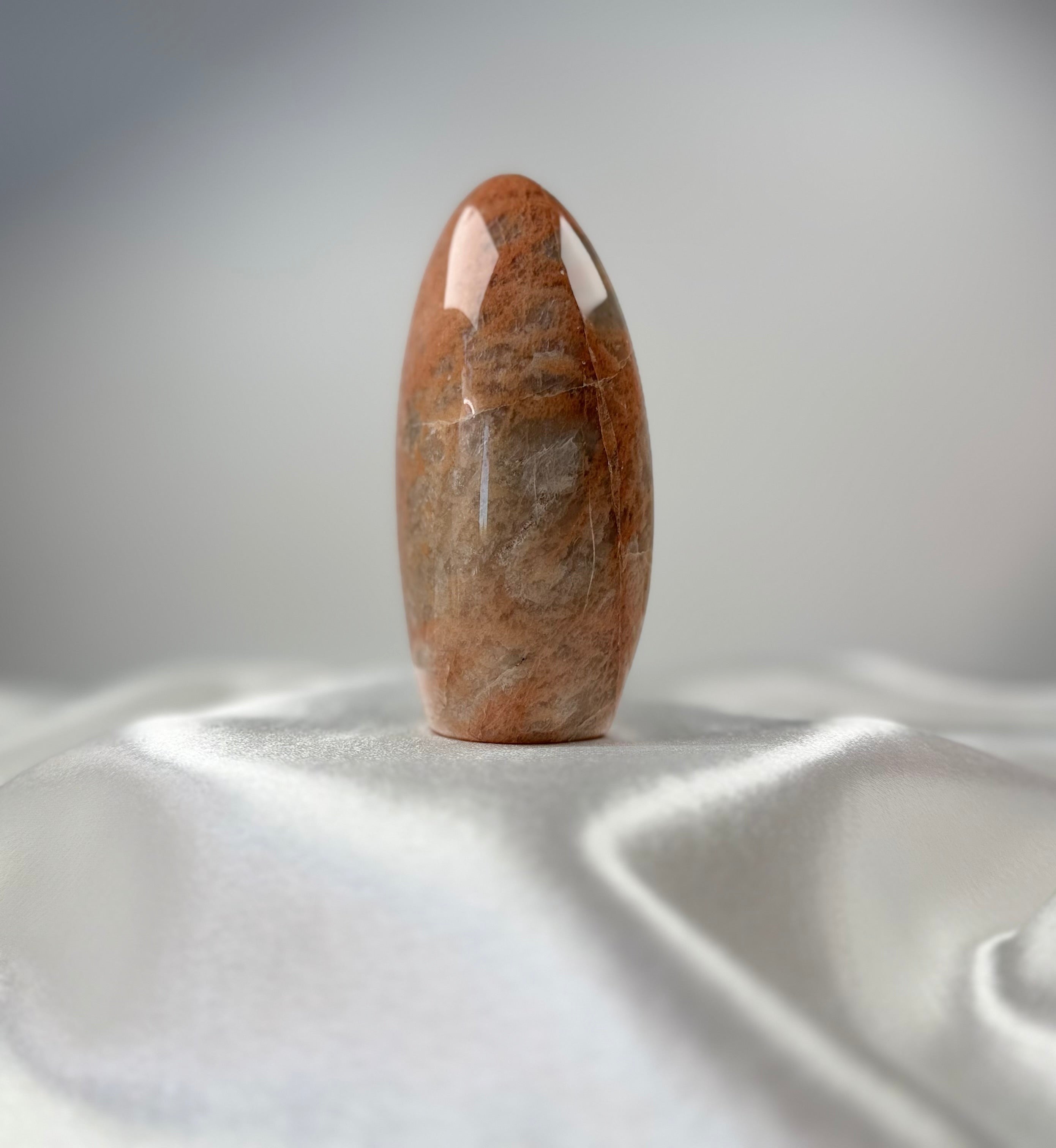 Treasured Energies polished peach moonstone crystal freeform with organic banding on a white satin cloth