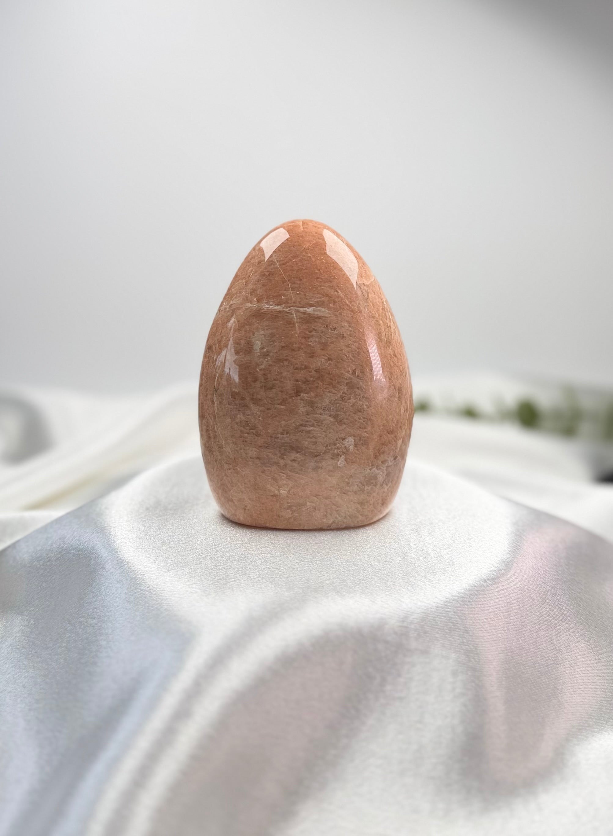 Treasured Energies polished peach moonstone crystal freeform with a smooth, organic shape on a white satin cloth.