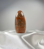Treasured Energies polished peach moonstone crystal freeform with organic banding on a white satin background.