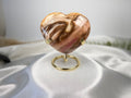 Treasured Energies polished petrified wood heart crystal displayed on a gold metal stand against a white satin cloth.
