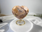 Treasured Energies polished petrified wood heart crystal on a gold metal display stand against a white satin cloth.