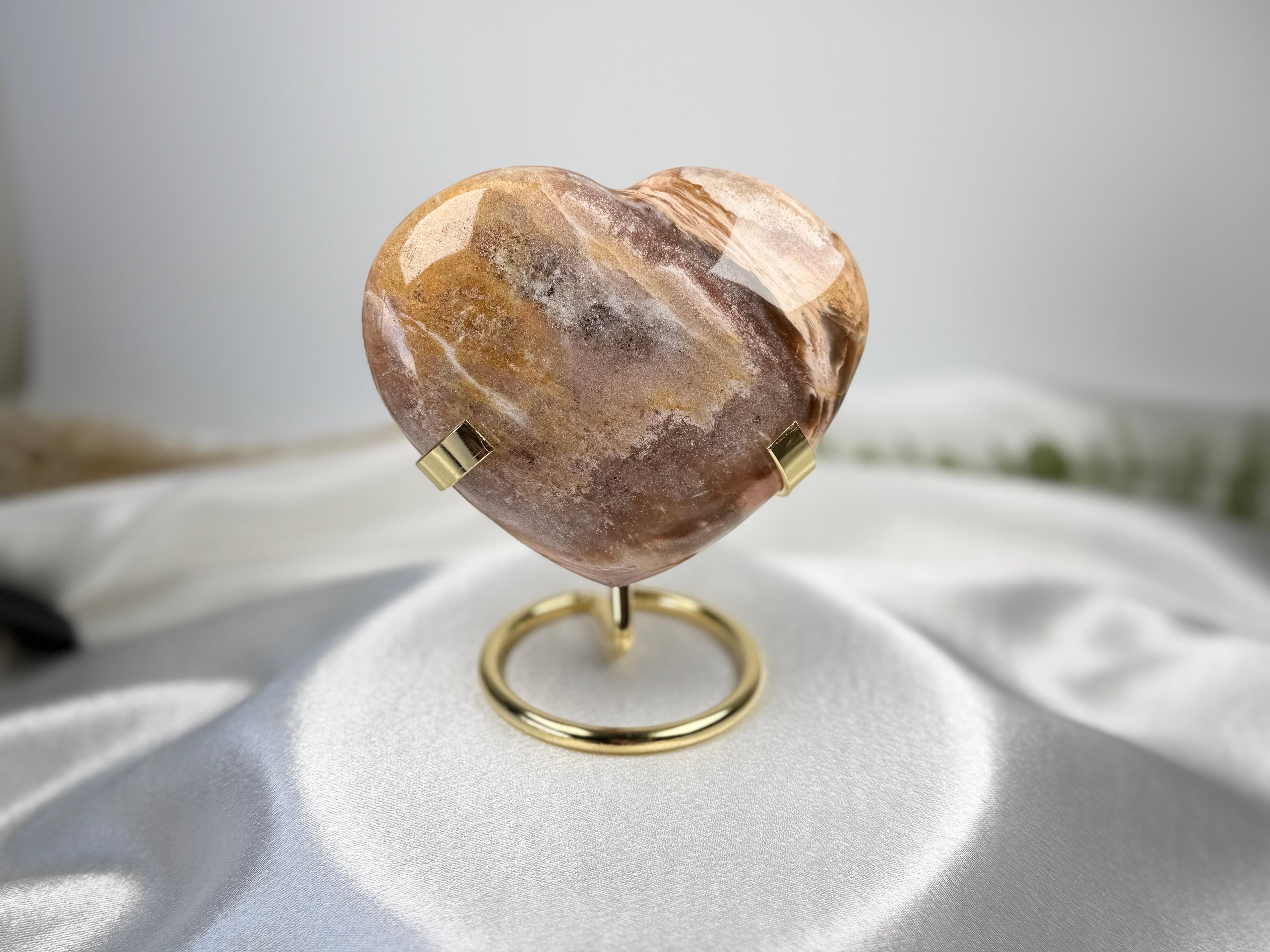 Treasured Energies polished petrified wood heart crystal on a gold metal display stand against a white satin cloth.