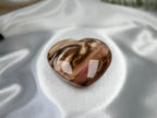 Treasured Energies polished petrified wood heart crystal with brown and cream wood grain patterns on white satin.