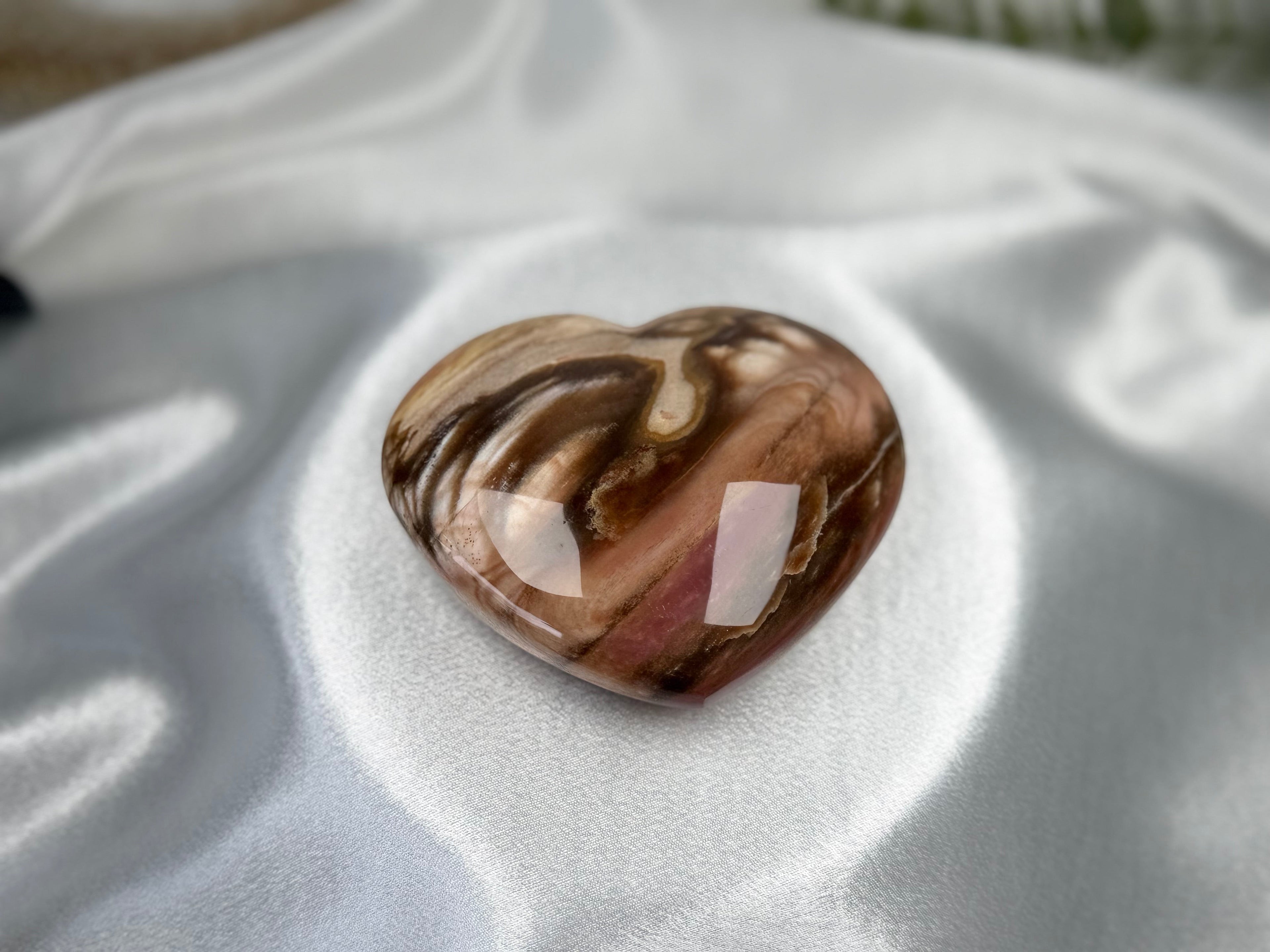 Treasured Energies polished petrified wood heart crystal with brown and cream wood grain patterns on white satin.