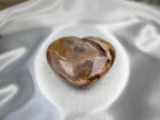 Treasured Energies polished petrified wood heart crystal with brown and cream wood grain patterns on white silk.