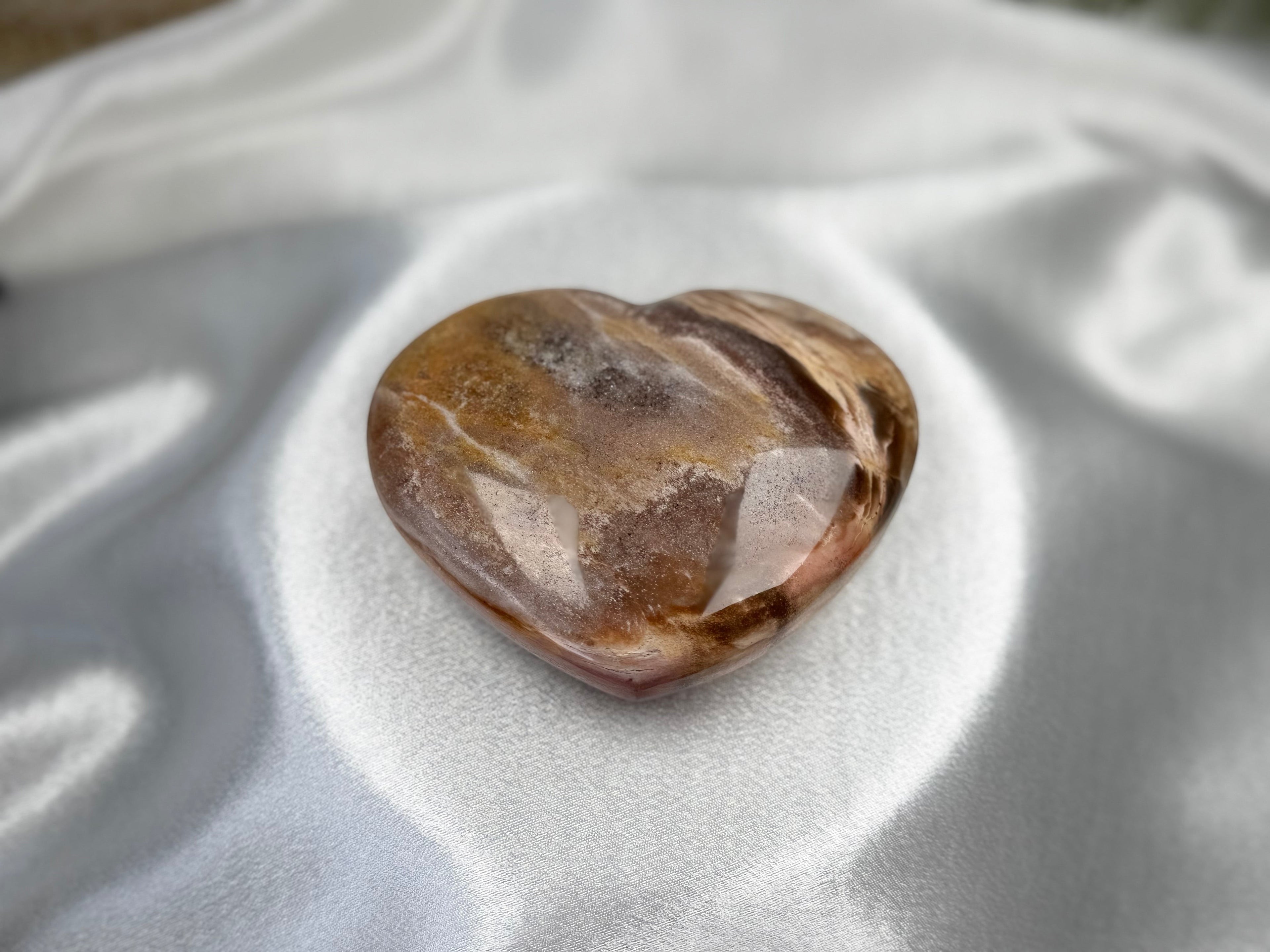 Treasured Energies polished petrified wood heart crystal with brown and cream wood grain patterns on white silk.