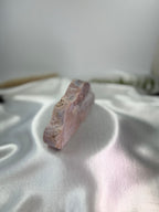Treasured Energies pink amethyst crystal specimen carved into a cloud shape resting on a white satin fabric background.