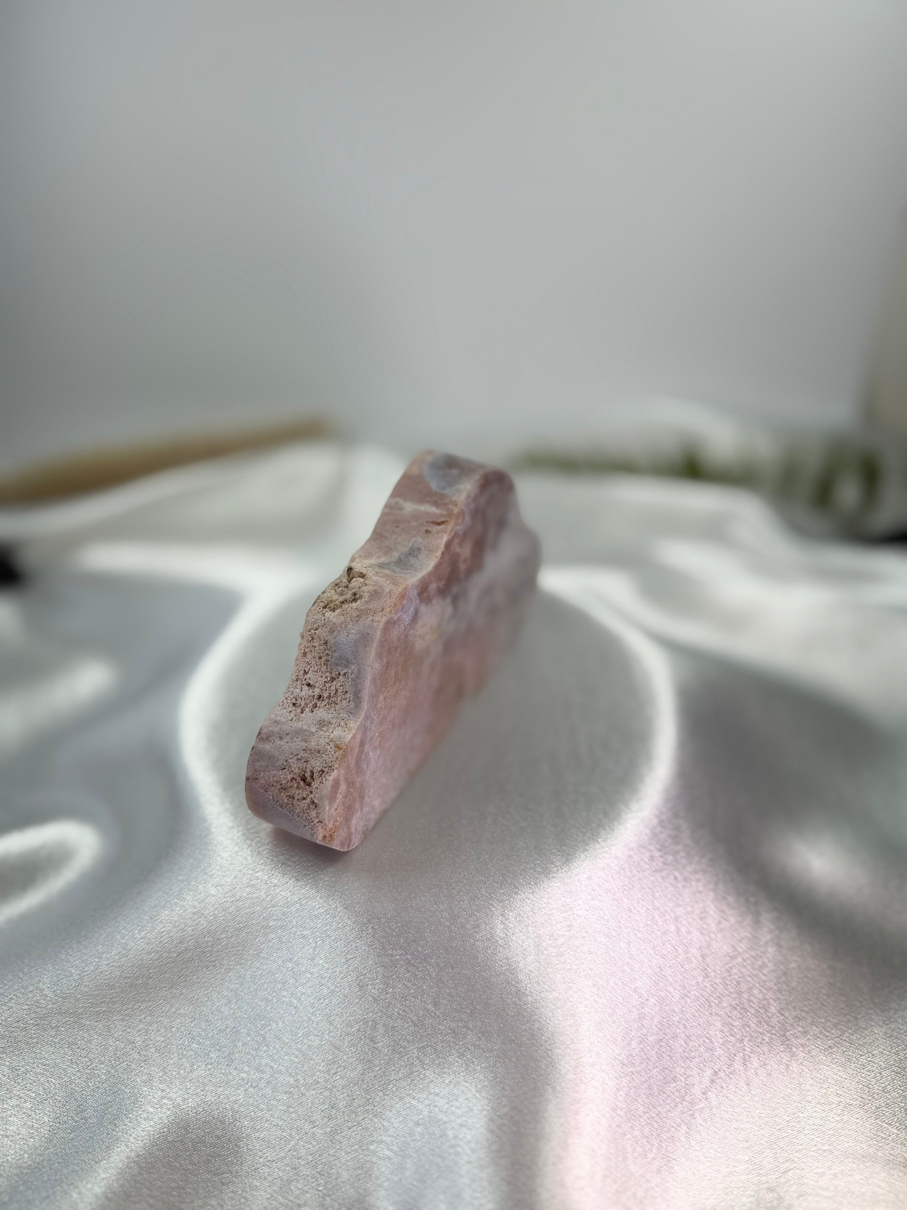 Treasured Energies pink amethyst crystal specimen carved into a cloud shape resting on a white satin fabric background.