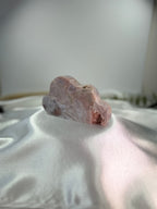 Treasured Energies pink amethyst crystal carved into a soft cloud shape, displayed on a white satin fabric.