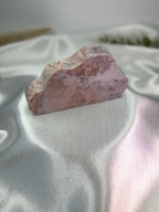 Treasured Energies pink amethyst crystal carved into a smooth cloud shape resting on a white satin fabric background.