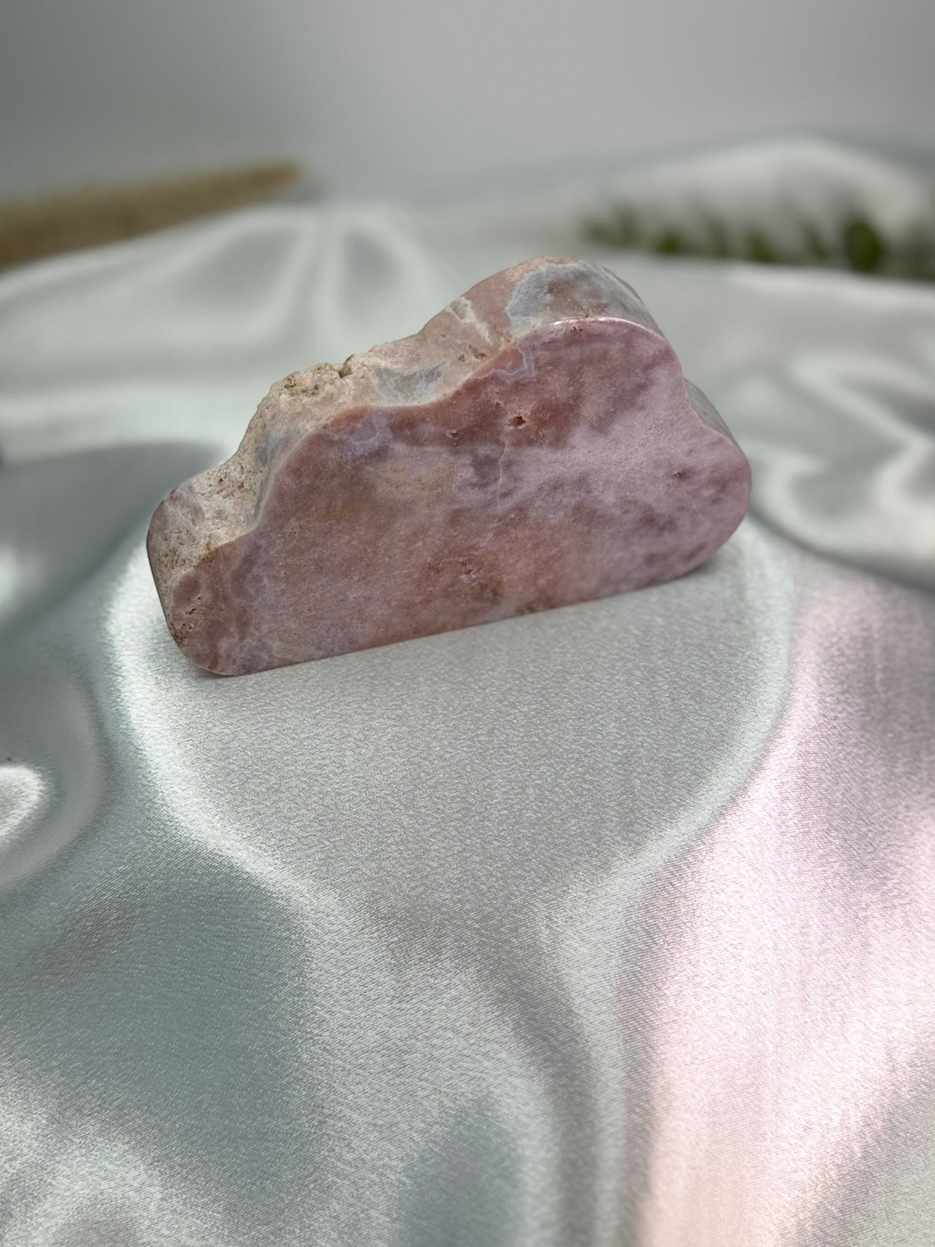 Treasured Energies pink amethyst crystal carved into a smooth cloud shape resting on a white satin fabric background.
