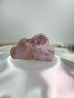Treasured Energies pink amethyst crystal carved into a smooth, whimsical cloud shape on a white satin background.