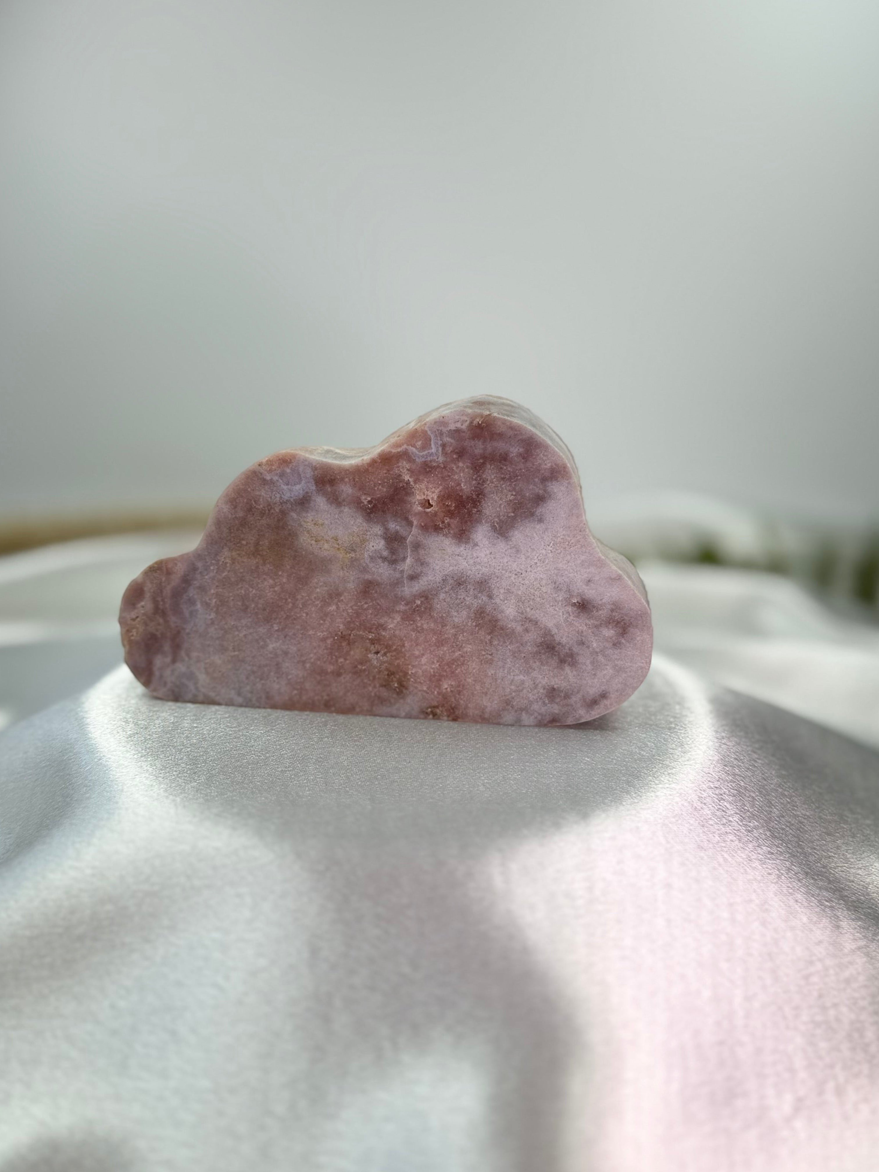 Treasured Energies pink amethyst crystal carved into a smooth, whimsical cloud shape on a white satin background.