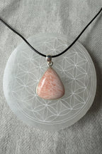 Treasured Energies scolecite crystal pendant in sterling silver on a black cord resting on a sacred geometry plate.