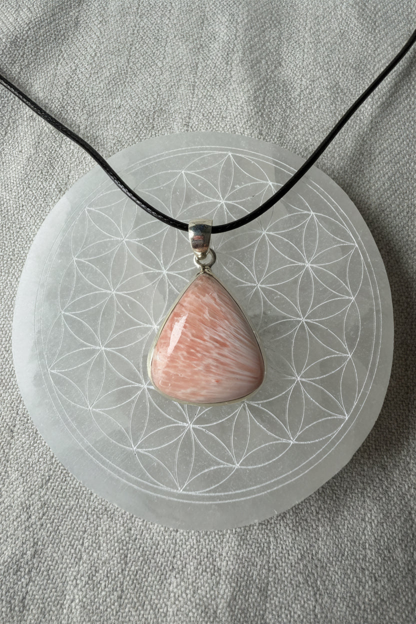 Treasured Energies scolecite crystal pendant in sterling silver on a black cord resting on a sacred geometry plate.