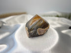 Treasured Energies polished agate crystal point with natural brown and grey banding on a white satin background.