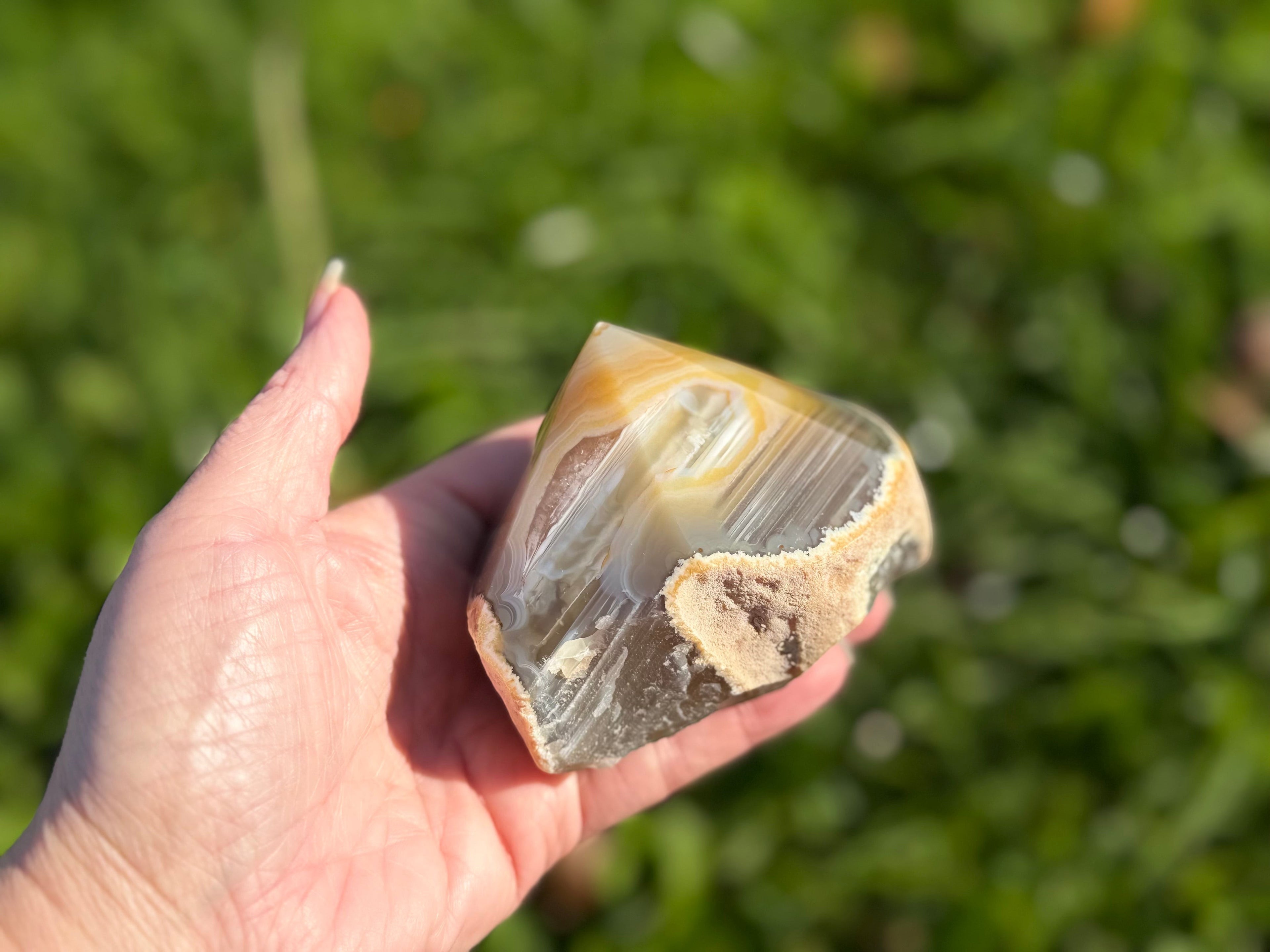 Treasured Energies polished agate crystal point held in hand against a blurred green outdoor background