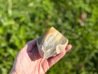 Treasured Energies polished agate point held in hand, showing natural brown and white banding against a green background.
