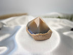 Treasured Energies polished agate point with smooth brown top and natural rough base on white satin fabric.