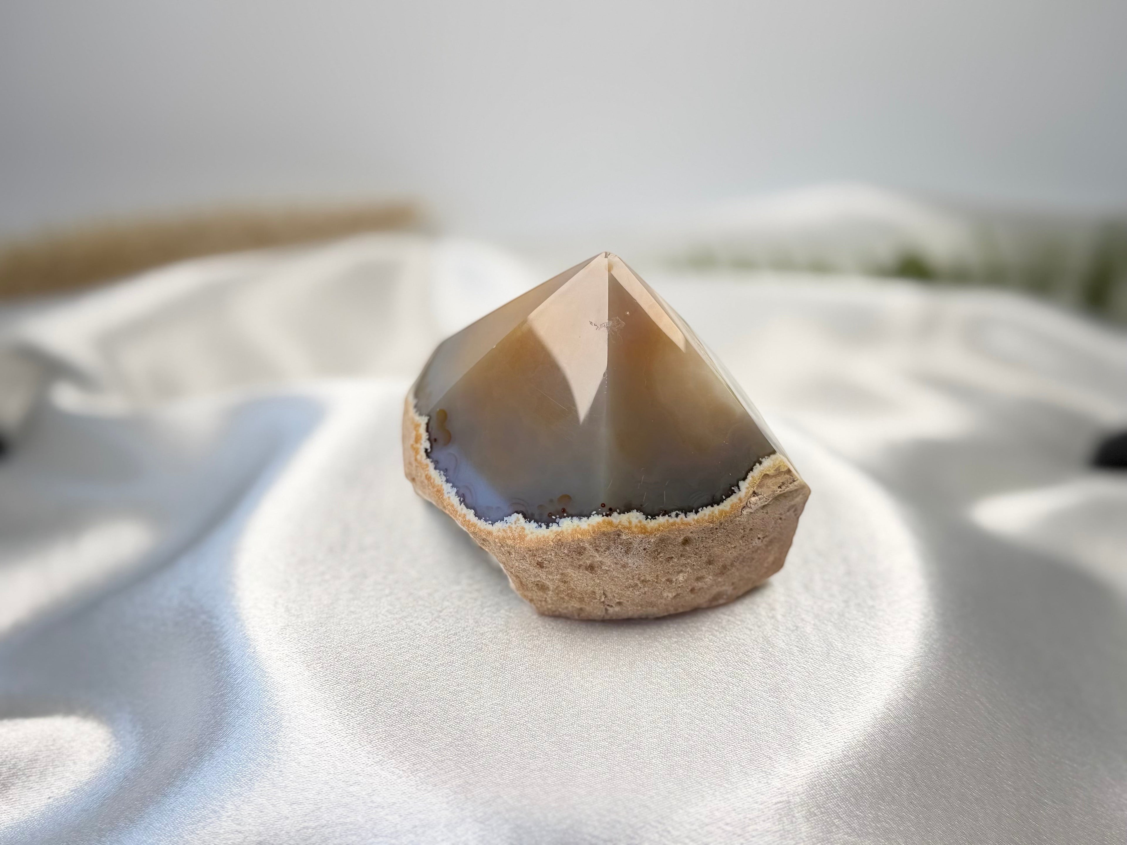 Treasured Energies polished agate point with smooth brown top and natural rough base on white satin fabric.