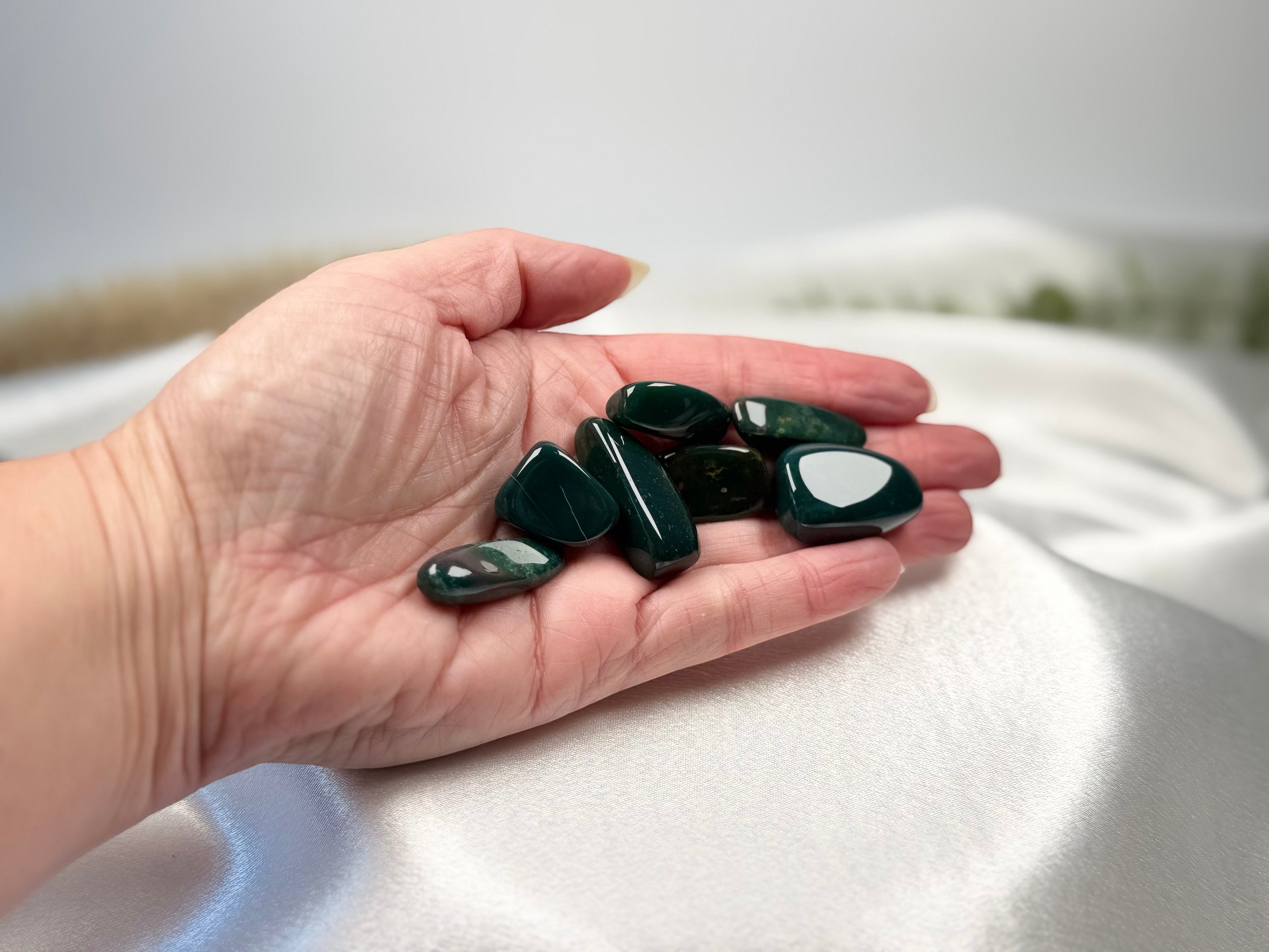 Treasured Energies polished bloodstone tumbled gemstones held in a hand against a soft white fabric background.