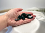 Treasured Energies polished natural bloodstone tumbled gemstones held in a palm against a soft white fabric background.